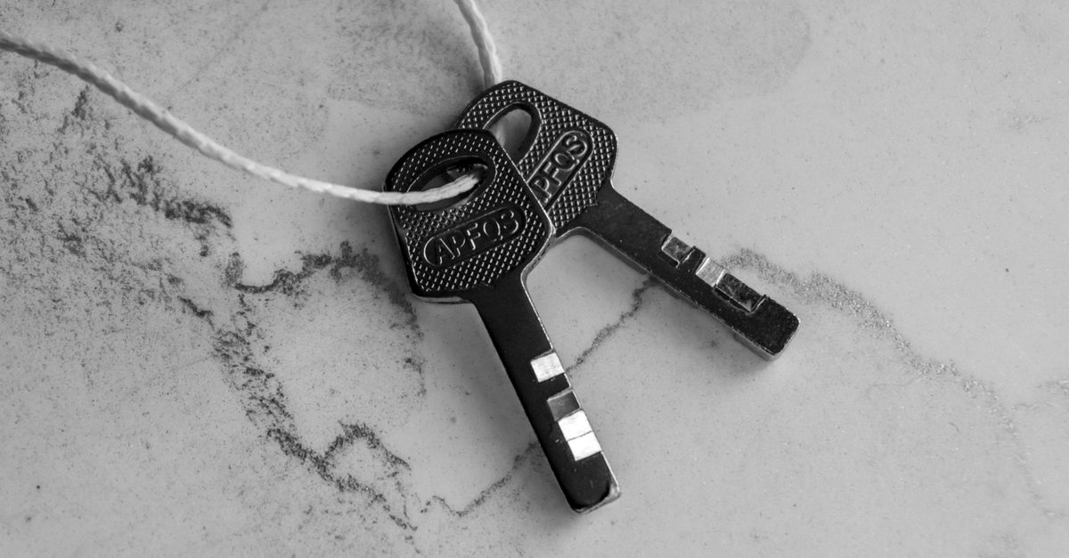 Black and white close-up of two keys tied with string on a textured marble surface.