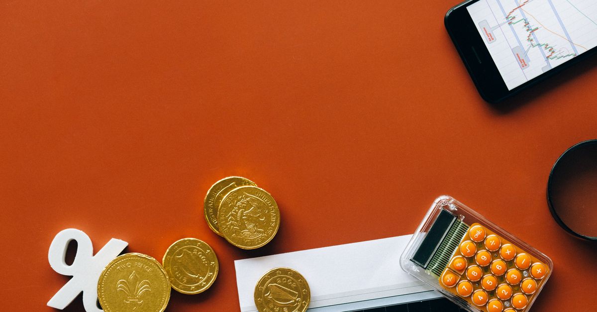 Flat lay showing coins, calculator, and charts on a red background for financial analysis and business concepts.